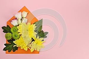 Composition of yellow, green Santini chrysanthemums and roses in an envelope on a pink background