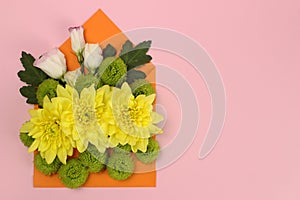 Composition of yellow, green Santini chrysanthemums and roses in an envelope on a pink background