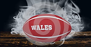 Compostion of rugby ball with text wales on black background with white blur