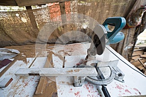 A compound miter saw placed on a work table with wood shaving and typical construction debris around it