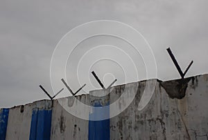 Compound wall and barbwire holders, dark clouds background