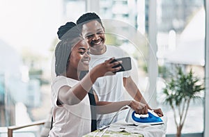 Compromise is key to a happy marriage. a happy young couple taking selfies while ironing freshly washed laundry together