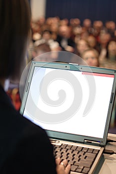 Moderátorka stojí v přední části velkého davu a zdá se, dává computer assisted prezentace.
