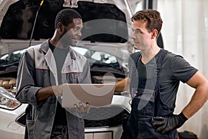 Computer Car Tuning. two Smiling auto mechanic testing a car engine connected to laptop.