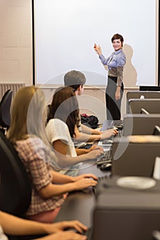 Computer class looking at teacher pointing on projection screen