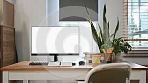 Computer, coffee cup, pencil holder and house plant on wooden table at home office.