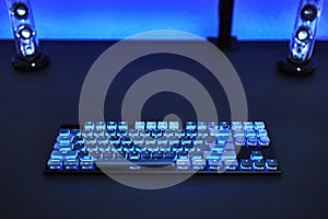 Computer desk with bright backlighted keyboard and stereo speakers. Blue color theme