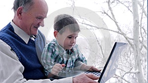 Computer game, grandpa with grandson with laptop in hand at home on window