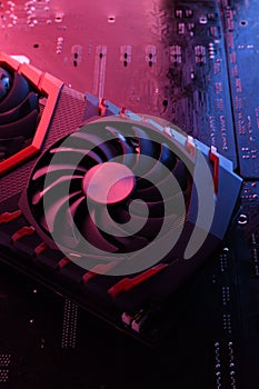 Computer game graphics card, videocard with two coolers on circuit board ,motherboard background. Close-up. With red-blue lighting