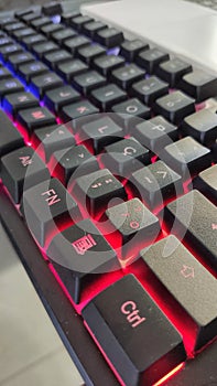 computer gamer keyboard with black keys on a gray table with keys illuminated in red and blue during the day with natural light