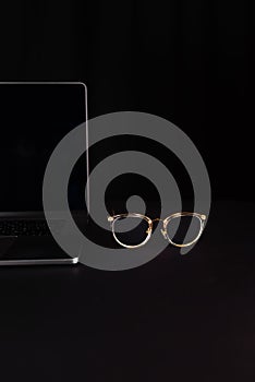 Computer glasses lie next to a laptop in low key