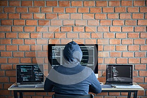 Computer hacker or cyber attack concept, Dangerous hooded hacker using multiple computers typing bad data into online system the