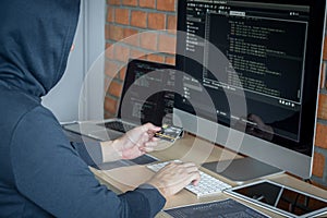 Computer hacker or cyber attack concept, Dangerous hooded hacker using multiple computers typing bad data into online system the