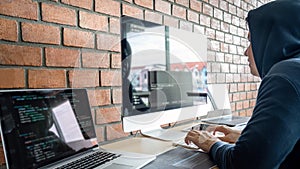 Computer hacker or cyber attack concept, Dangerous hooded hacker using multiple computers typing bad data into online system the