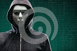 Computer hacker in mask and hoodie over abstract binary background. Obscured dark face. Data thief, internet fraud