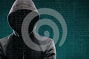 Computer hacker in mask and hoodie over abstract binary background. Obscured dark face. Data thief, internet fraud