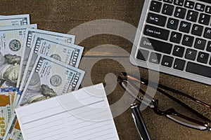 Computer keyboard with dollar money on notepad, pen and glasses wooden table