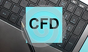 The computer keyboard has a pen and a blue sticker with the text CFD Contract for Difference. Flat lay