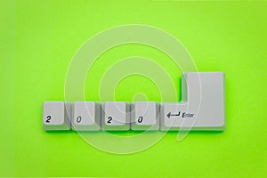 Computer keyboard keys with 2020 enter written using the white buttons on green background. New year technology concept