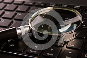 Computer keyboard and magnifying glass, close-up. Computer security concept