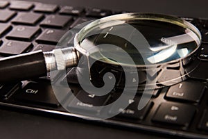 Computer keyboard and magnifying glass, close-up. Computer security concept