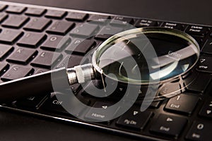 Computer keyboard and magnifying glass, close-up. Computer security concept