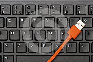 Computer keyboard and orange USB cable for data transfer