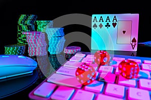 Computer keyboard and quads of four aces, illuminated with pink light on black background. Cards, casino chips and dice