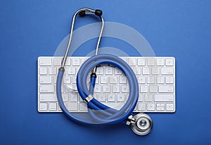 Computer keyboard with stethoscope on blue background, top view