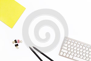 Computer keyboard, a yellow pad, two black pencil and clips for paper on white background. Minimal business concept of office work