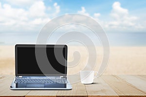 Computer laptop with black screen and hot coffee cup on wooden table top on blurred beach background