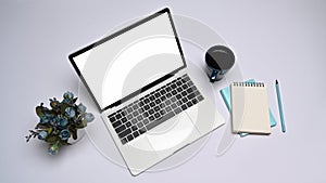 Computer laptop, coffee cup, notepad and flower pot on white table.