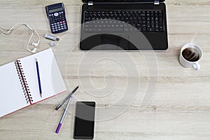 Computer laptop with mobile phone, office supplies and hot black coffee cup with steam on vintage wooden desk background