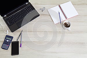 Computer laptop with mobile phone, office supplies and hot black coffee cup with steam on vintage wooden desk background