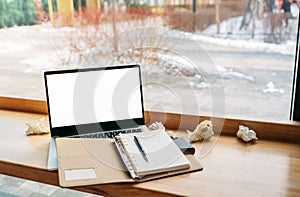 Computer laptop with white blank screen putting together with notebook and on the modern wooden table with windows in cafe as