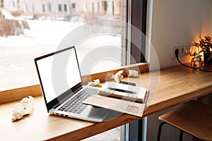 Computer laptop with white blank screen putting together with notebook and on the modern wooden table with windows in cafe as