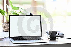 A computer laptop with a white blank screen is putting on a white working desk.