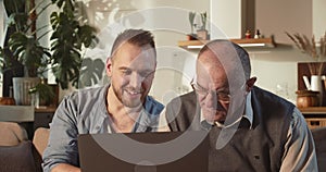 Computer literacy for older people. Happy Caucasian young adult man teaching to use senior dad to use laptop at home.