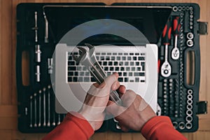 Computer maintenance repair concept of man technician holding chrome socket wrench spanner on background with silver laptop on