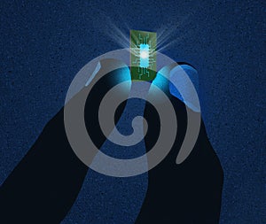 A computer microchip glows with light as it is held in dark fingertips on a dark grunge background