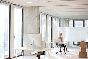 Computer monitor on desk with businesswoman working in background at office