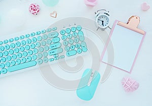 Computer mouse and keyboard in mint white, pink clipboard, paper clip, candle, alarm clock, pink paper flower on a white table. Fl