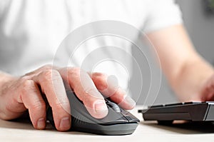 A computer mouse in a man& x27;s hand and a black keyboard. Closeup