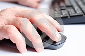 A computer mouse in a man& x27;s hand and a black keyboard. White background.