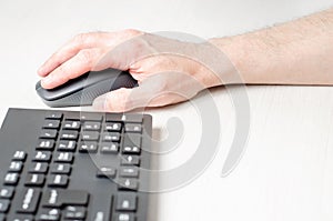 A computer mouse in a man's hand and a black keyboard. White background