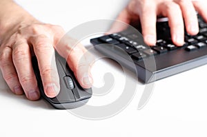 A computer mouse in a man& x27;s hand and a black keyboard. White background.