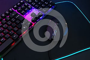 Computer mouse, mousepad and RGB keyboard on dark background, closeup