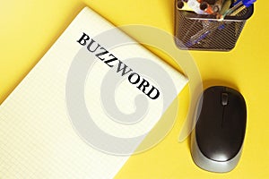 Computer mouse, pens, felt-tip pens, notepad with text BUZZWORD on a yellow background