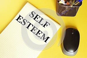 Computer mouse, pens, felt-tip pens, notepad with text Self Esteem on a yellow background