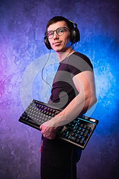 Computer nerd with keyboard over colorful pink and blue neon lit wall